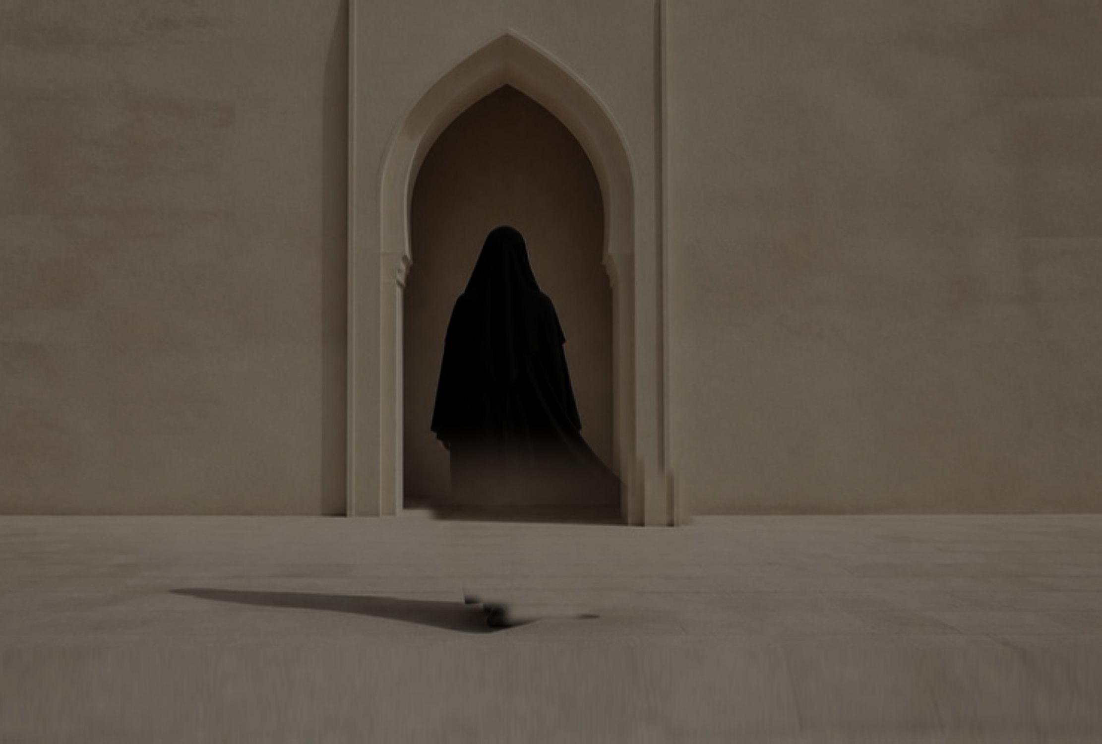 A woman in a flowing black abaya walking towards a sandstone arch